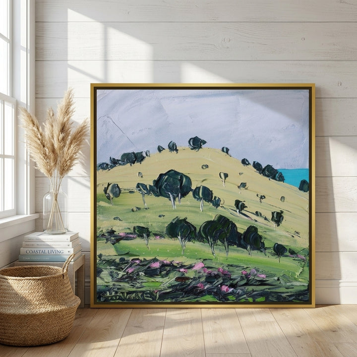 Oversized statement canvas wall art with a gold leaf surround leaning against the wall in a coastal bedroom