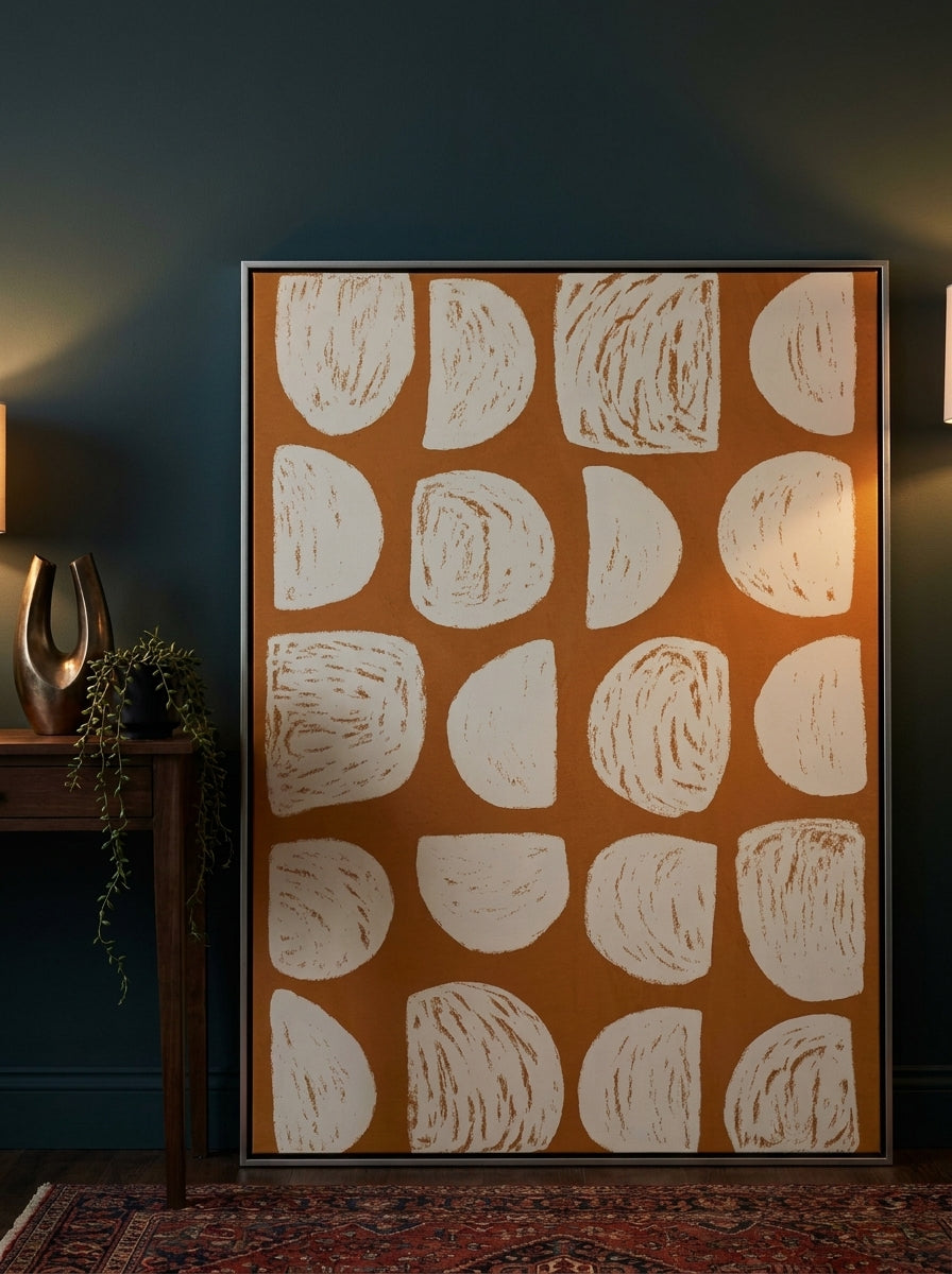 Oversized statement canvas wall art with a silver leaf surround leaning against the wall in a moody dining room