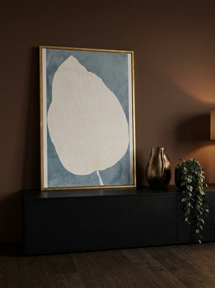 Canvas wall art with a gold leaf surround standing on a console in a moody bedroom