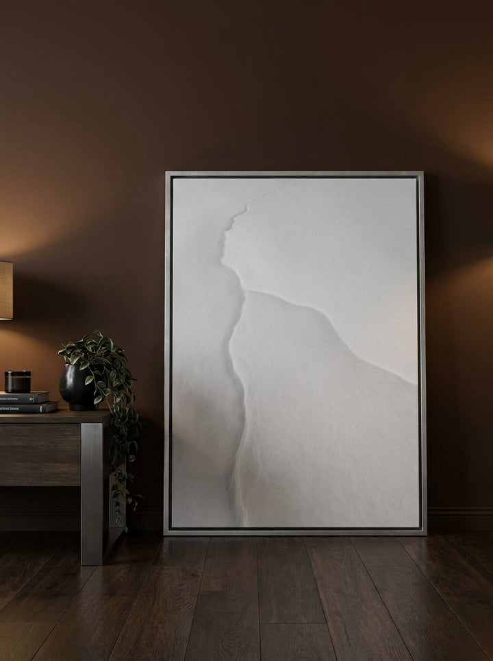 Oversized statement canvas wall art with a silver leaf surround leaning against the wall in a moody living room