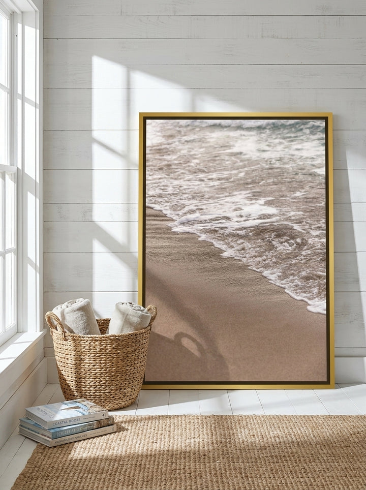 Oversized statement canvas wall art with a gold leaf surround leaning against the wall in a coastal bedroom
