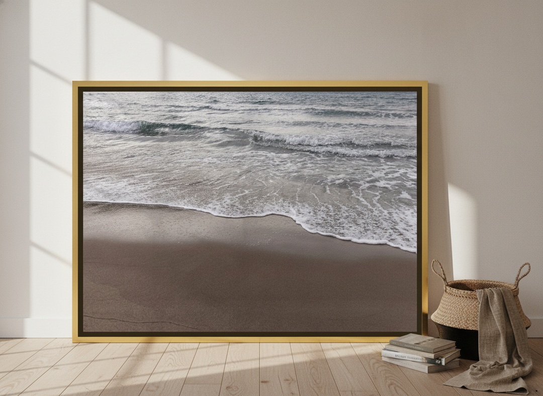 Oversized statement canvas wall art with a gold leaf surround leaning against the wall in a coastal bedroom