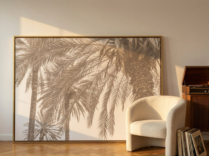 Oversized statement canvas wall art with a gold leaf surround leaning against the wall in a mid-century living room