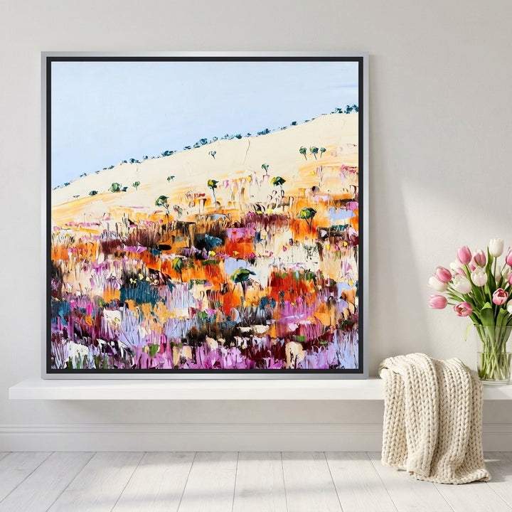 Canvas wall art with a silver leaf surround standing on a shelf in a bright Scandinavian living room