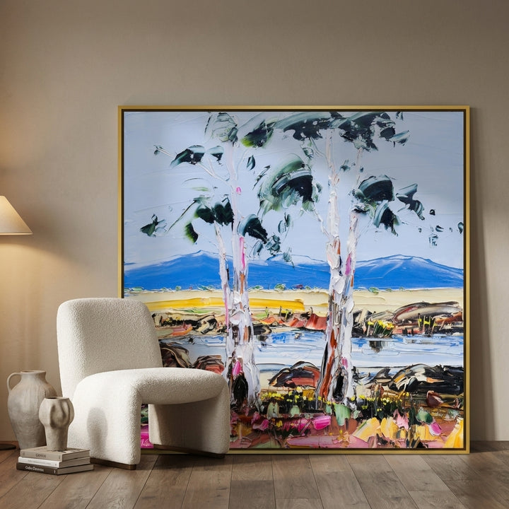 Oversized statement canvas wall art with a gold leaf surround leaning against the wall in a luxe living room