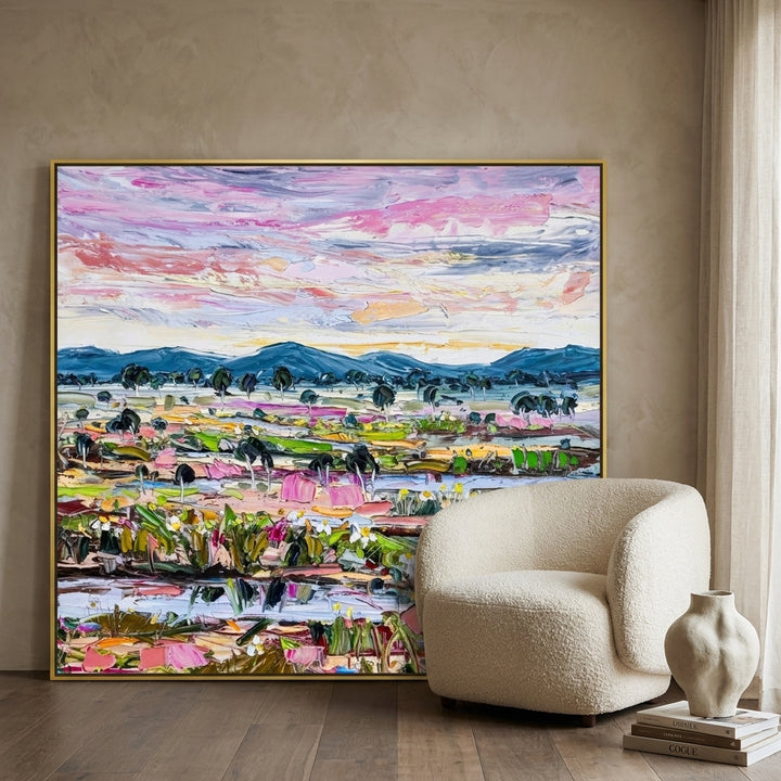 Oversized statement canvas wall art with a gold leaf surround leaning against the wall in a luxe living room