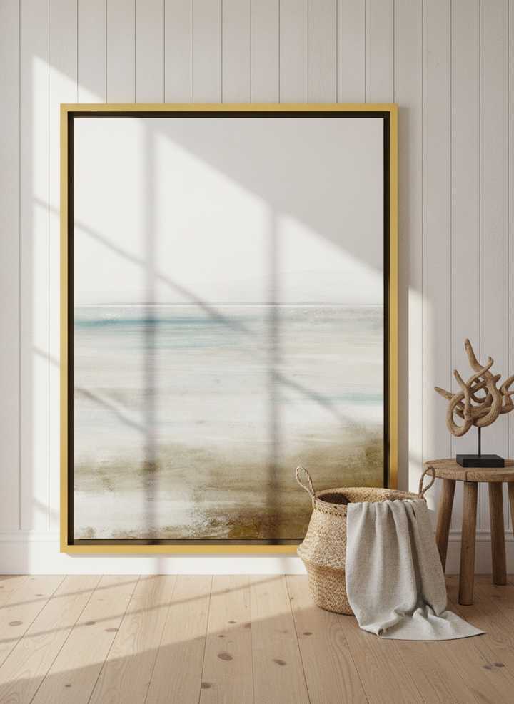 Oversized statement canvas wall art with a gold leaf surround leaning against the wall in a coastal bedroom