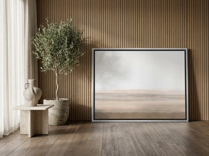 Oversized statement canvas wall art with a silver leaf surround leaning against the wall in a luxe living room