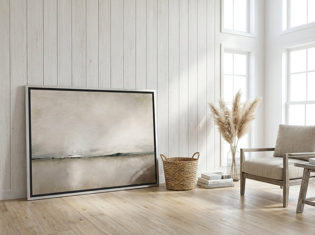 Oversized statement canvas wall art with a silver leaf surround leaning against the wall in a coastal living room
