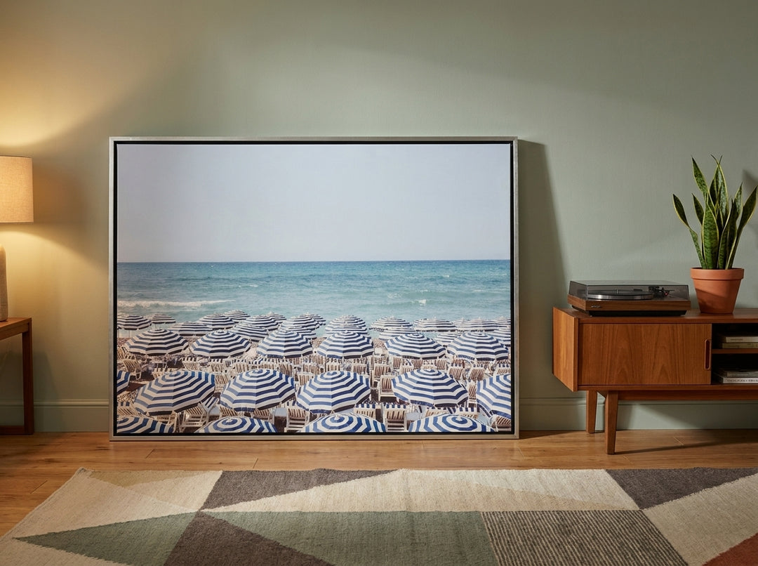 Oversized statement canvas wall art with a silver leaf surround leaning against the wall in a mid-century living room