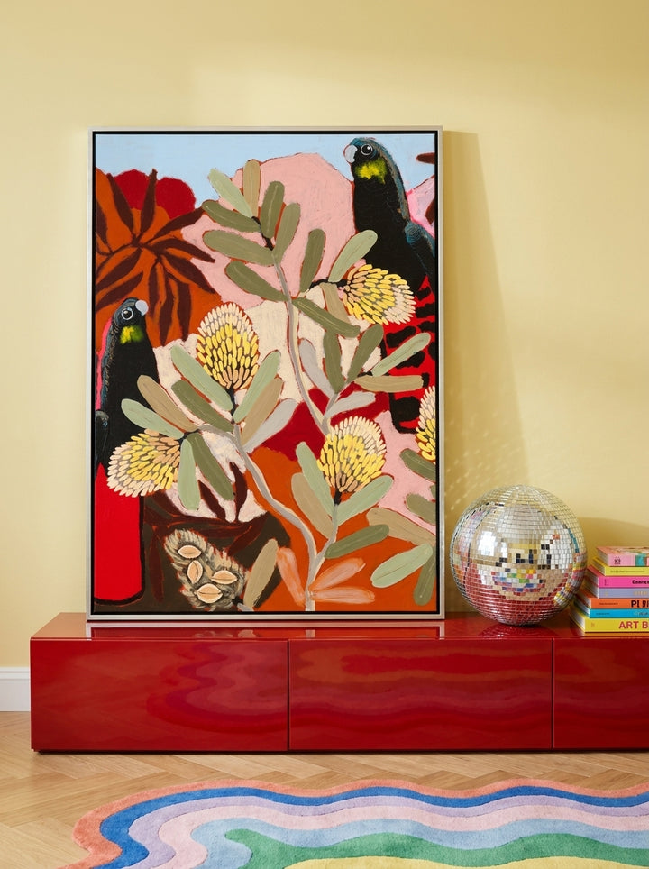 Canvas wall art with a silver leaf surround standing on a sideboard in a colourful eclectic bedroom