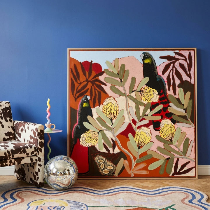 Oversized statement canvas wall art with a natural timber surround leaning against the wall in a colourful eclectic dining room