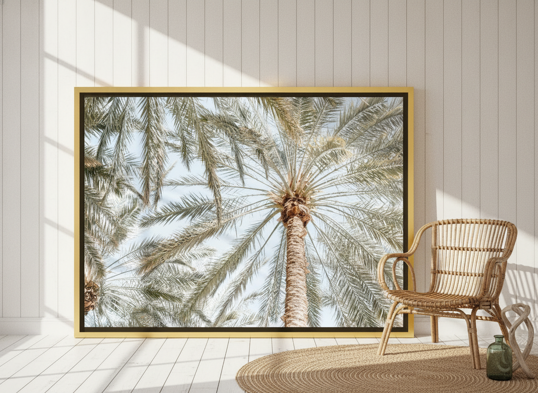 Oversized statement canvas wall art with a gold leaf surround leaning against the wall in a coastal dining room