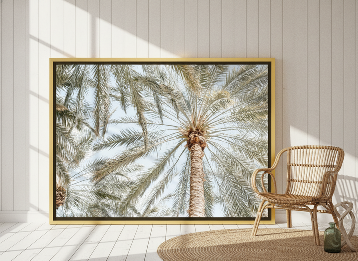 Oversized statement canvas wall art with a gold leaf surround leaning against the wall in a coastal dining room