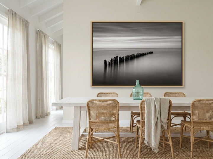 Oversized statement canvas wall art with a natural timber surround styled on the wall in a coastal dining room