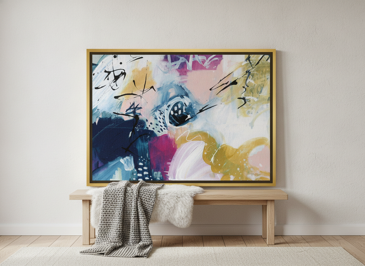 Canvas wall art with a gold leaf surround standing on a bench in a bright Scandinavian bedroom