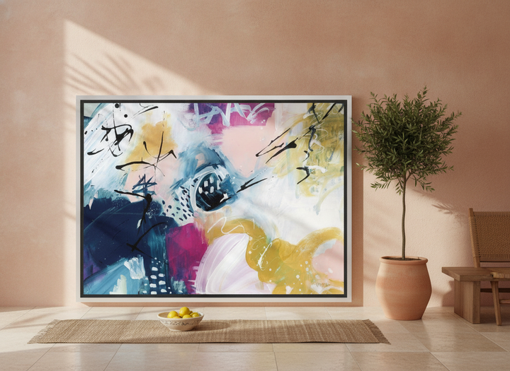 Oversized statement canvas wall art with a silver leaf surround leaning against the wall in a Mediterranean dining room