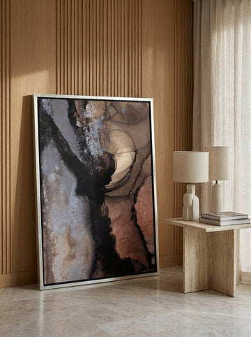 Oversized statement canvas wall art with a silver leaf surround leaning against the wall in a luxe bedroom