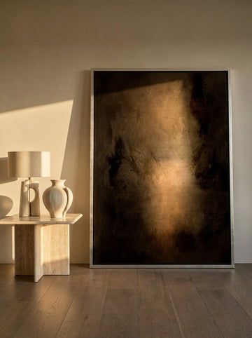 Oversized statement canvas wall art with a silver leaf surround leaning against the wall in a luxe dining room