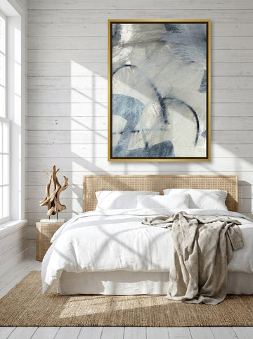 Canvas wall art with a gold leaf surround styled on the wall in a coastal bedroom