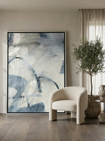 Oversized statement canvas wall art with a silver leaf surround leaning against the wall in a luxe dining room