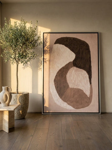 Oversized statement canvas wall art with a silver leaf surround leaning against the wall in a luxe bedroom