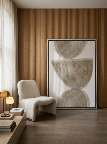 Oversized statement canvas wall art with a silver leaf surround leaning against the wall in a luxe living room