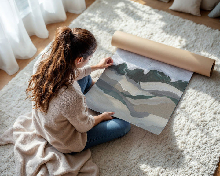Person unrolling a large sheet of paper with a mountain design on a carpeted floor.