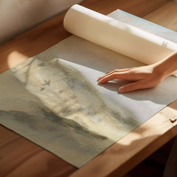 Hand unrolling a piece of paper with a landscape design on a wooden surface