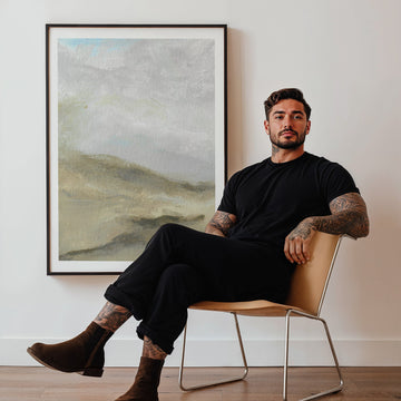 Man sitting on a chair in a room with a landscape painting on the wall.