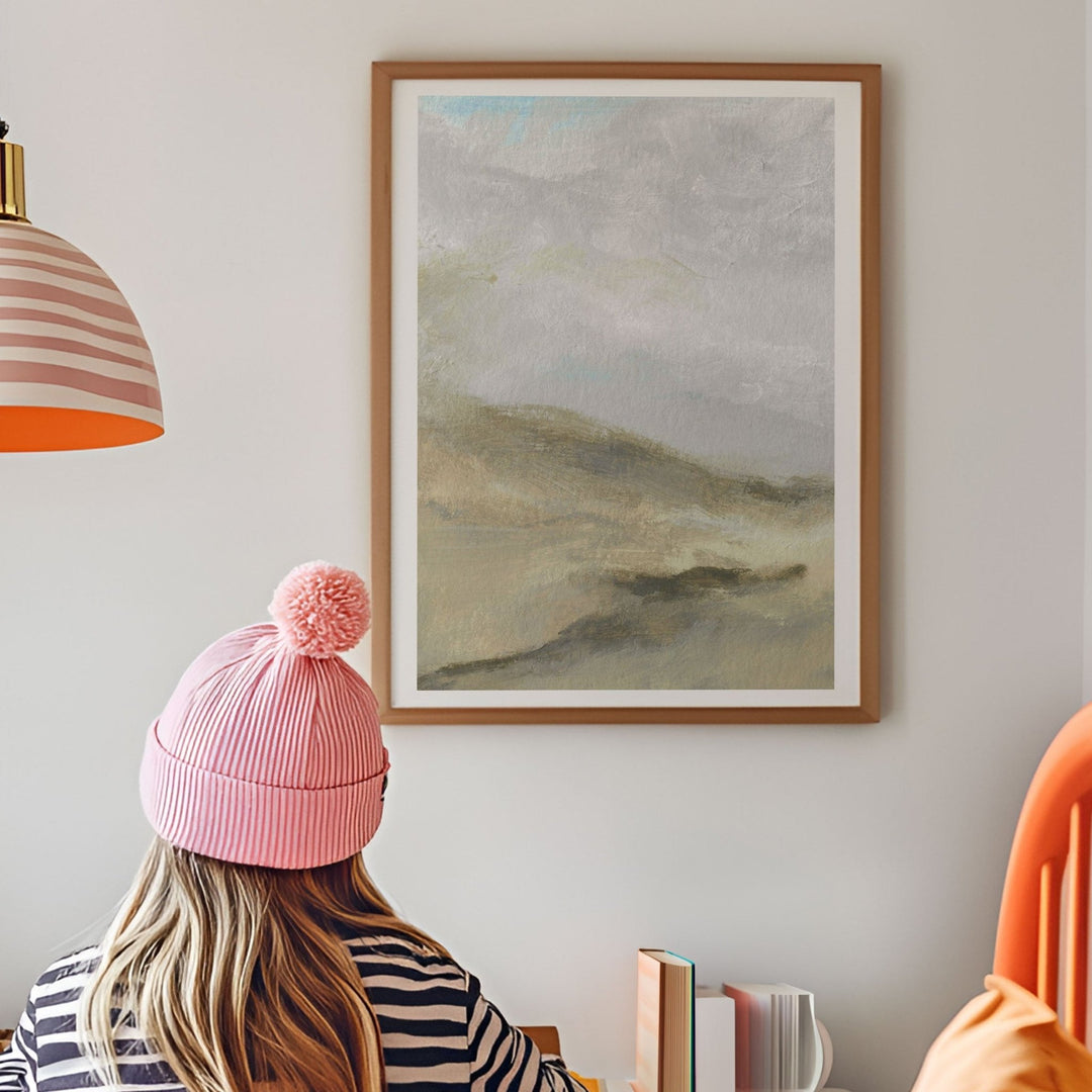 Person wearing a pink beanie sitting at a desk with a landscape painting on the wall.