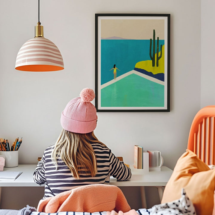 Person wearing a pink beanie sitting at a desk with a colorful painting on the wall.