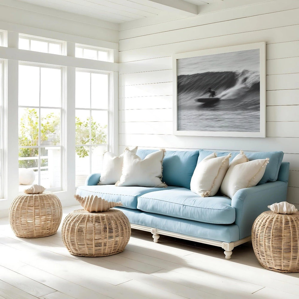 Light blue sofa with white and beige cushions in a bright room with large windows and a picture of a wave.
