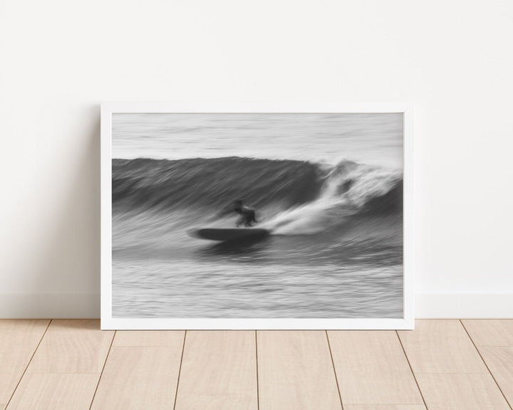 Black and white photograph of a surfer on a wave in a minimalistic room.