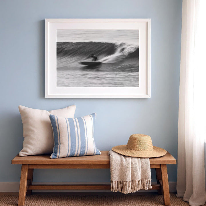 Artwork of a surfer on a wave above a wooden bench with pillows and a hat.