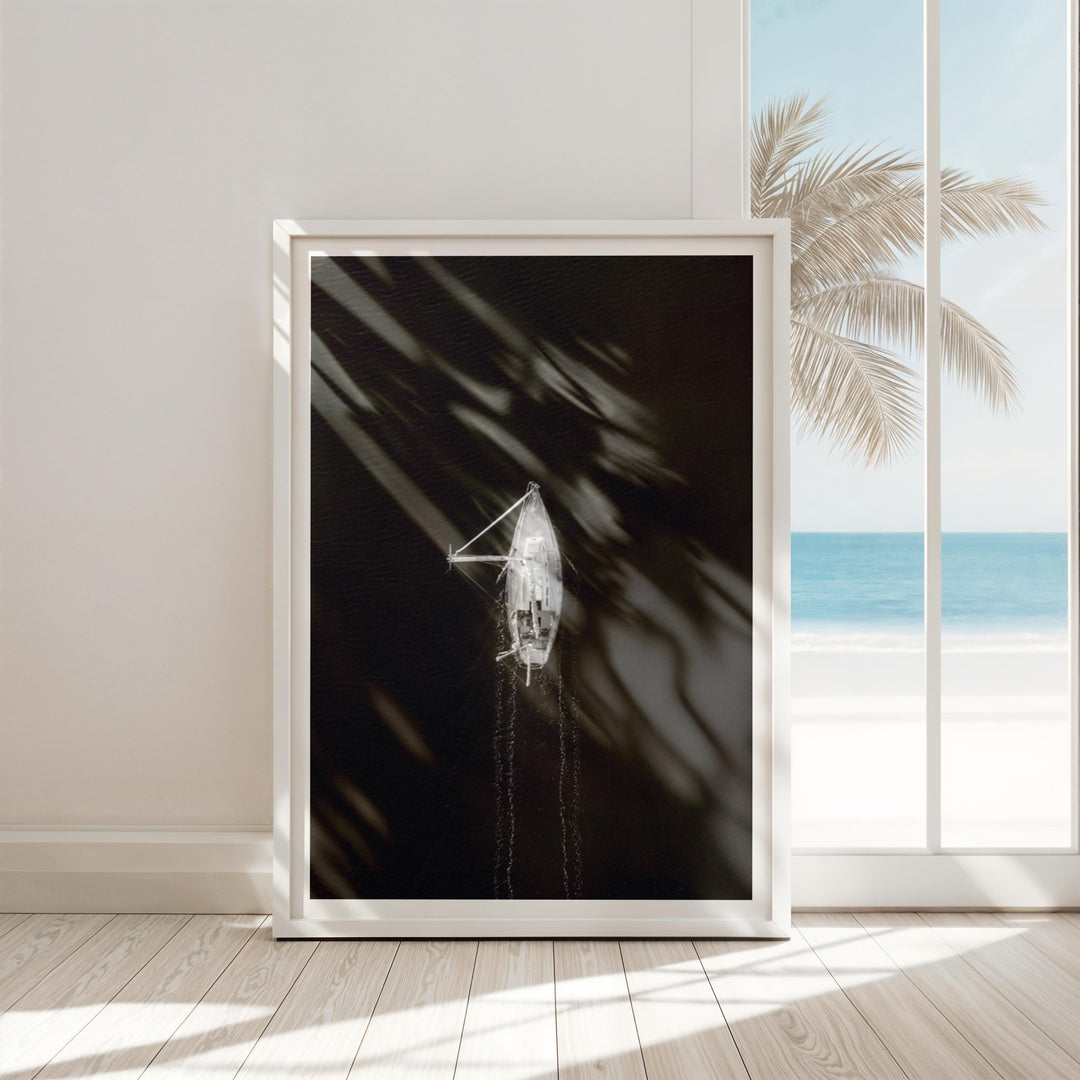 artwork of a boat on a dark background with palm leaves, displayed in a room with a window view of the ocean.