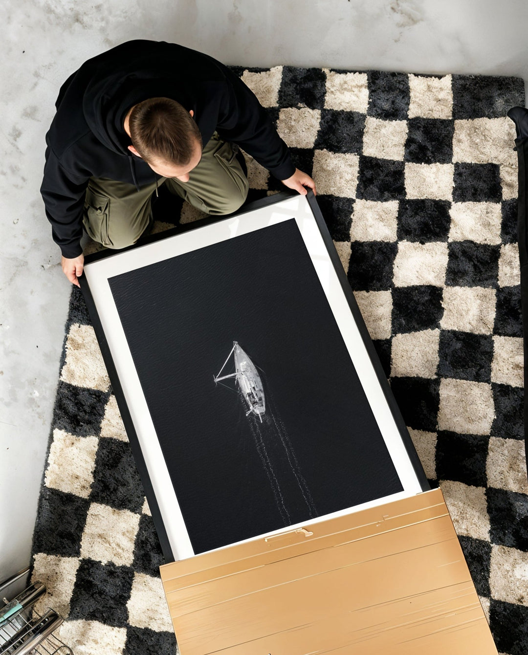 Person unboxing a large black and white photograph on a checkered rug.