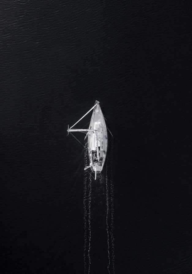 Aerial view of a sailboat on a dark body of water framed