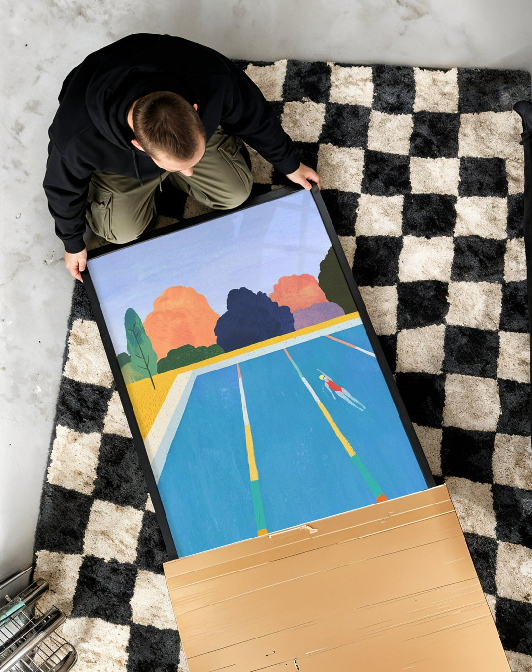 Person unboxing a colorful abstract painting on a checkered rug.