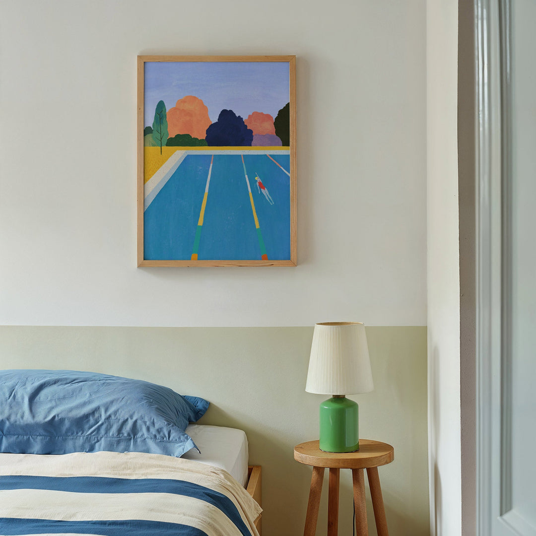 artwork above a bed with a lamp on a side table.