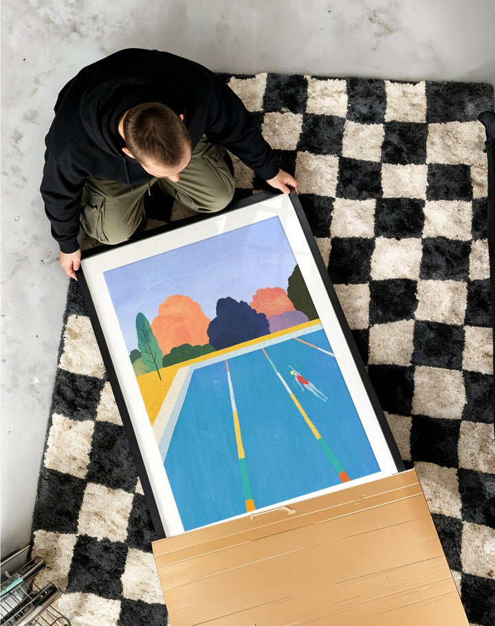 Person unboxing a colorful abstract painting on a checkered rug.