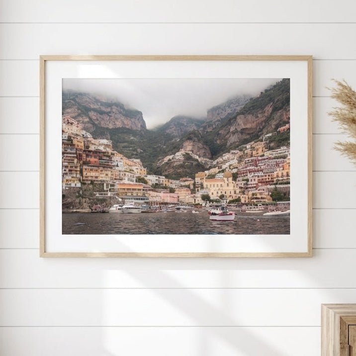 Artwork of a mountain village on a white wall with a wooden side table and basket below.