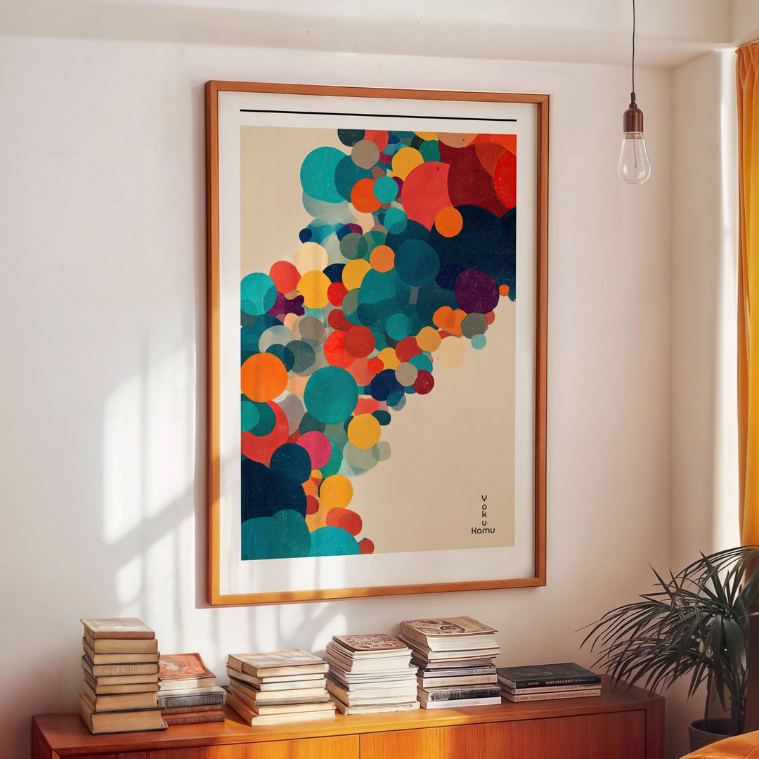 Colorful abstract art print in a wooden picture on a wall above a wooden cabinet with books.