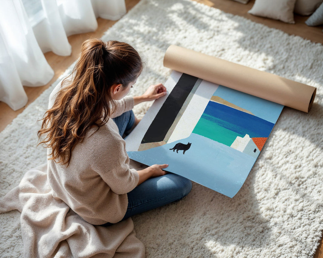 Woman sitting on a carpeted floor unrolling a large poster with a scenic design.