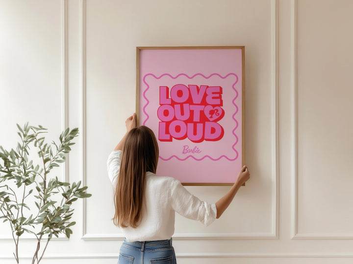 Person hanging a pink poster with 'Love Out Loud' text on a wall.