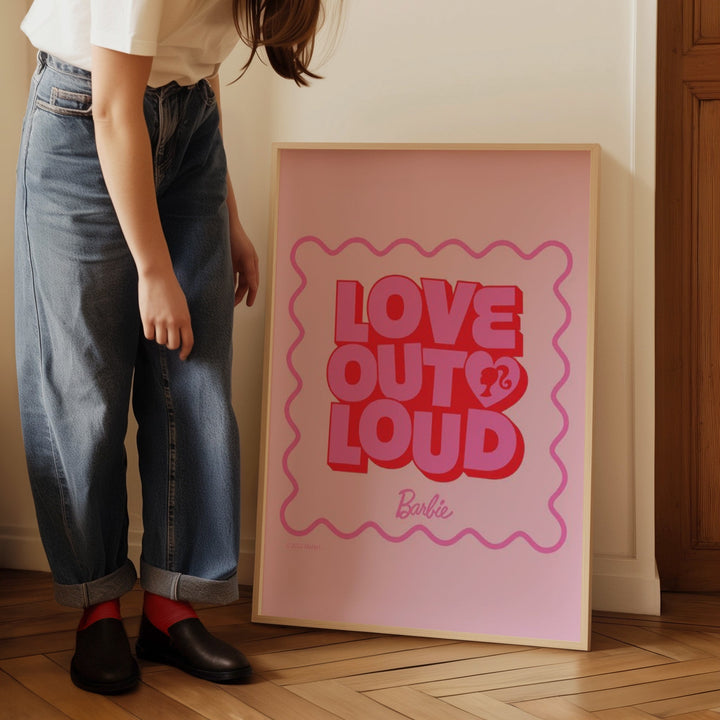 Person standing next to a 'Love Out Loud' Barbie poster on a wooden floor.