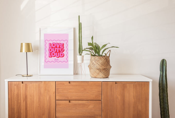 Wooden cabinet with a pink poster, lamp, and plants on a white wall.