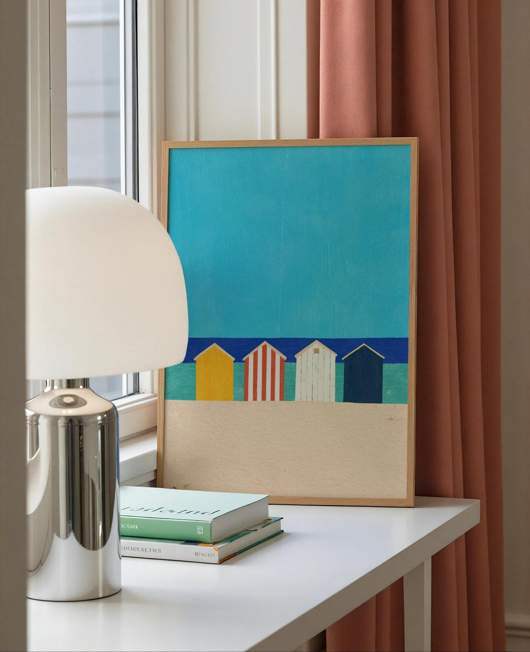 Colorful artwork on a table with a lamp and books, against a window and pink curtain.