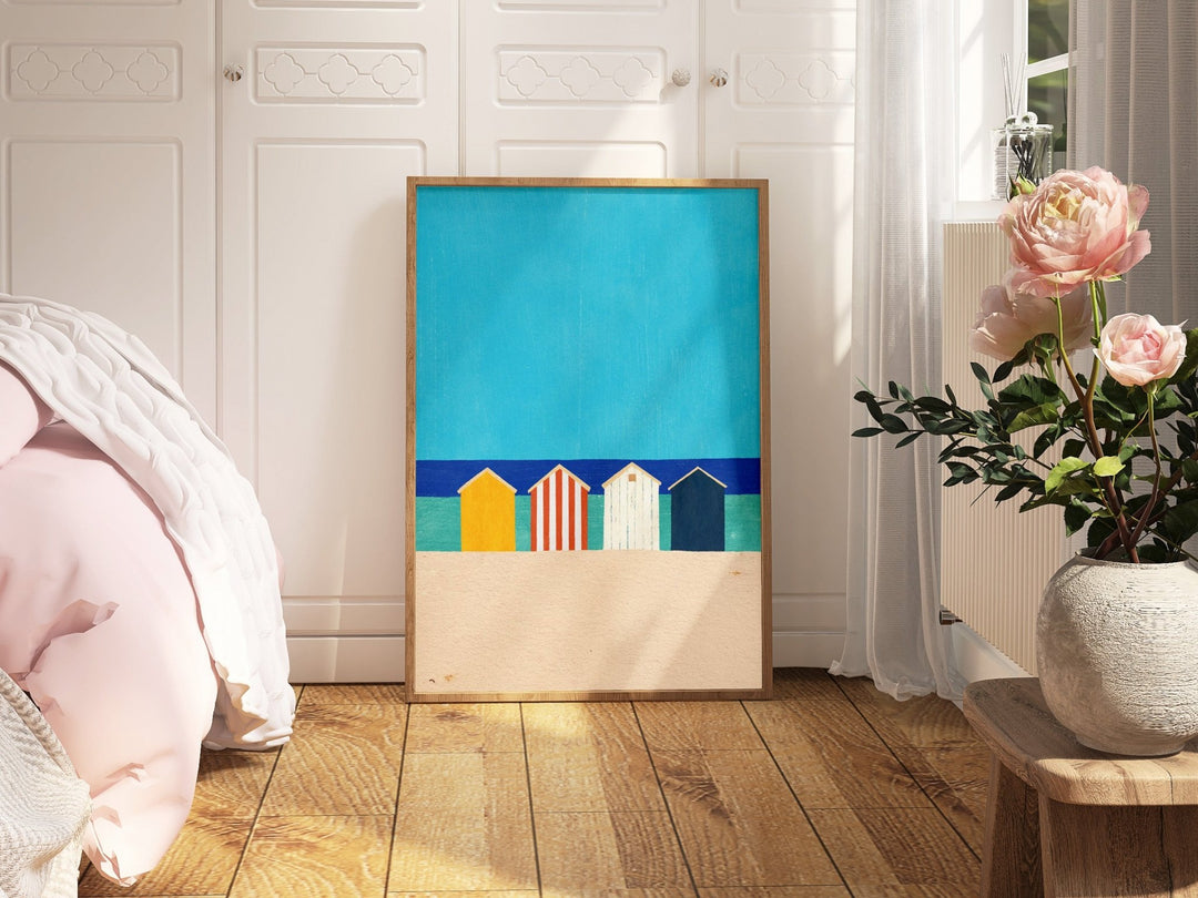 Artwork with colorful houses on a blue background in a room with a bed and flowers.