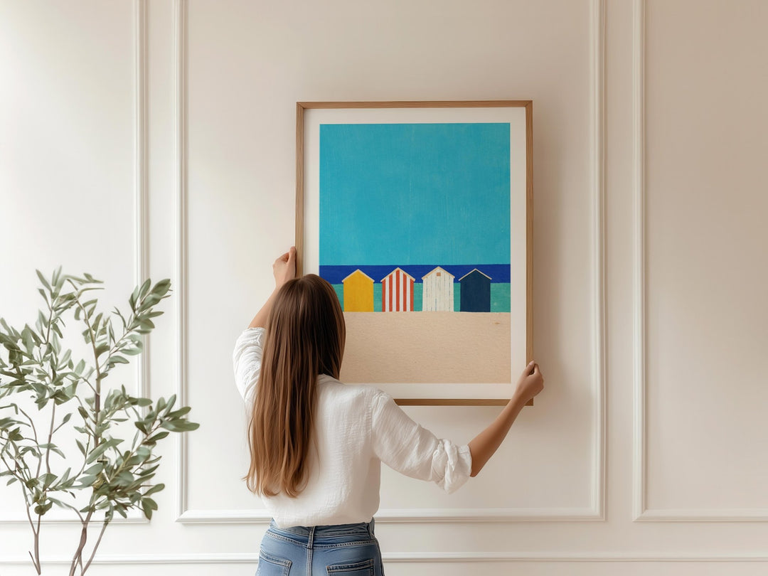 Person hanging artwork of colorful beach huts on a wall.